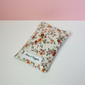 Floral-patterned pouch with 'Pins & Giggles' label on a white surface and pink background