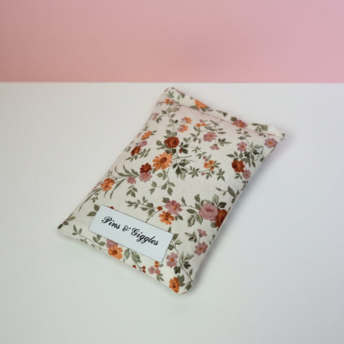 Floral-patterned pouch with 'Pins & Giggles' label on a white surface and pink background
