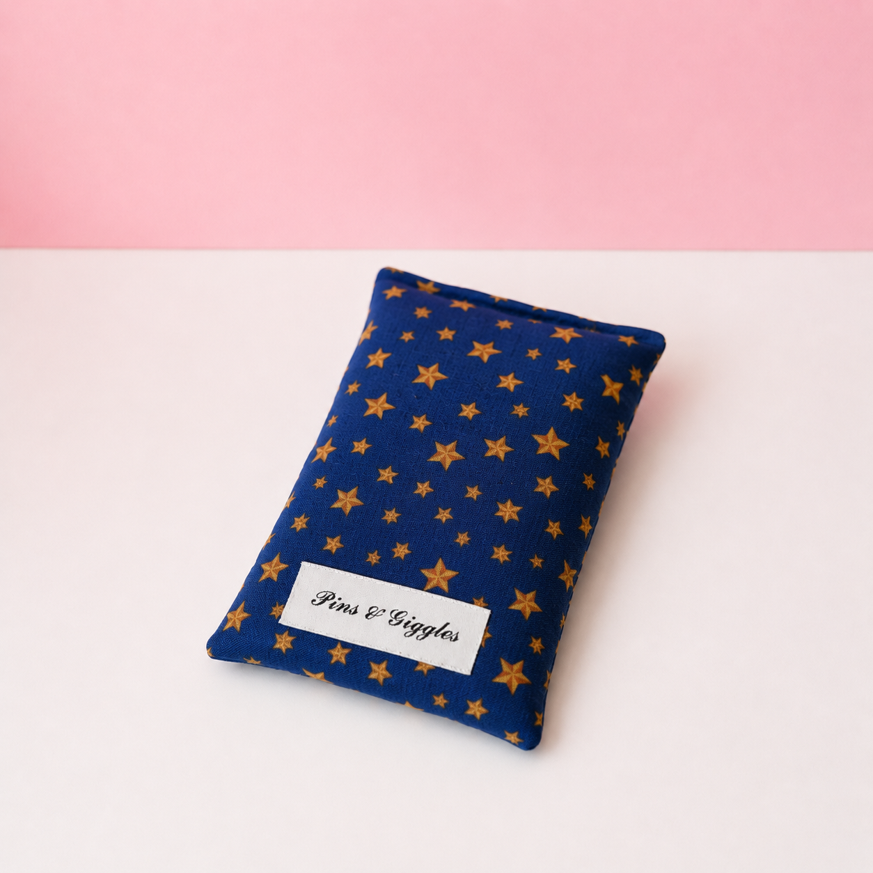 Blue fabric pouch with yellow star pattern and 'Pins & Giggles' label on a white surface