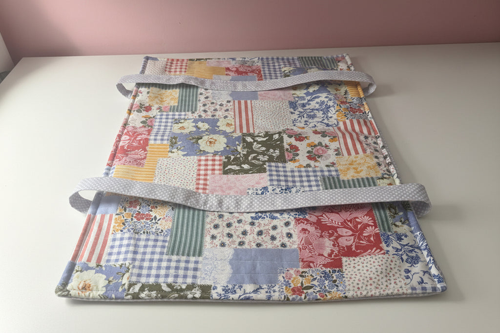A patchwork fabric casserole carrier laying flat on a white table. 
