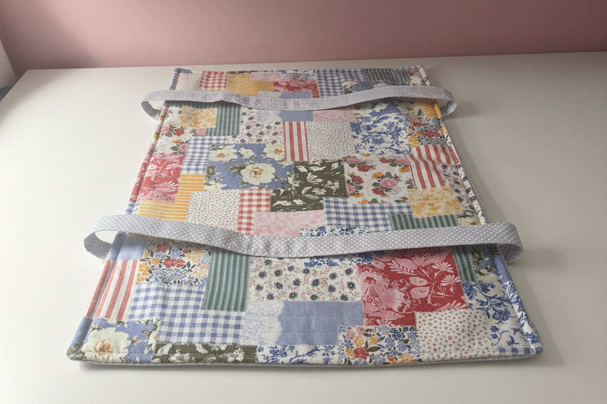 A patchwork fabric casserole carrier laying flat on a white table. 
