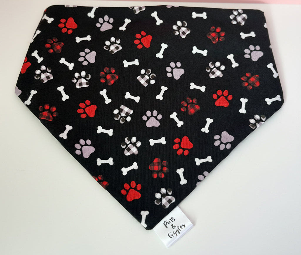 Black bandana with red, white, and gray paw print pattern on a wooden surface.