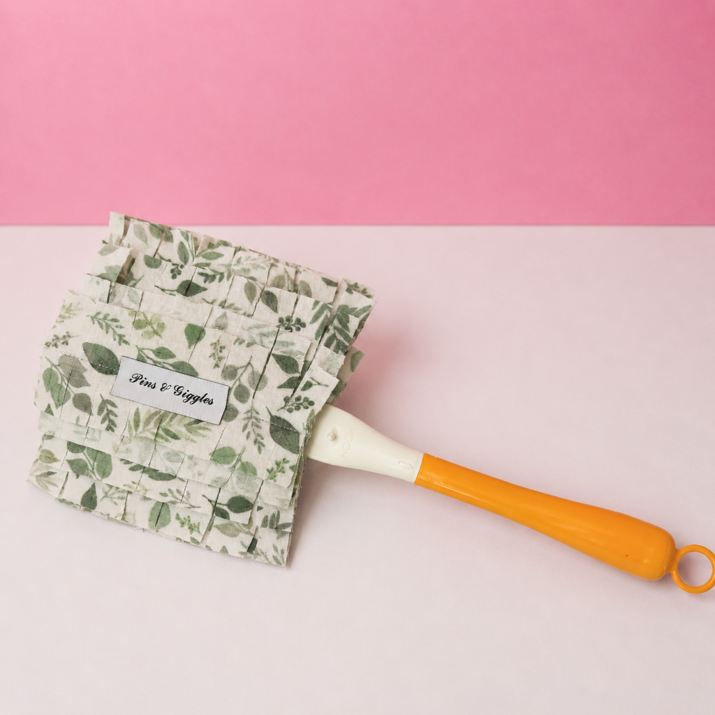 Leaf-patterned swiffer duster cover with a yellow-handle on a pink and white background