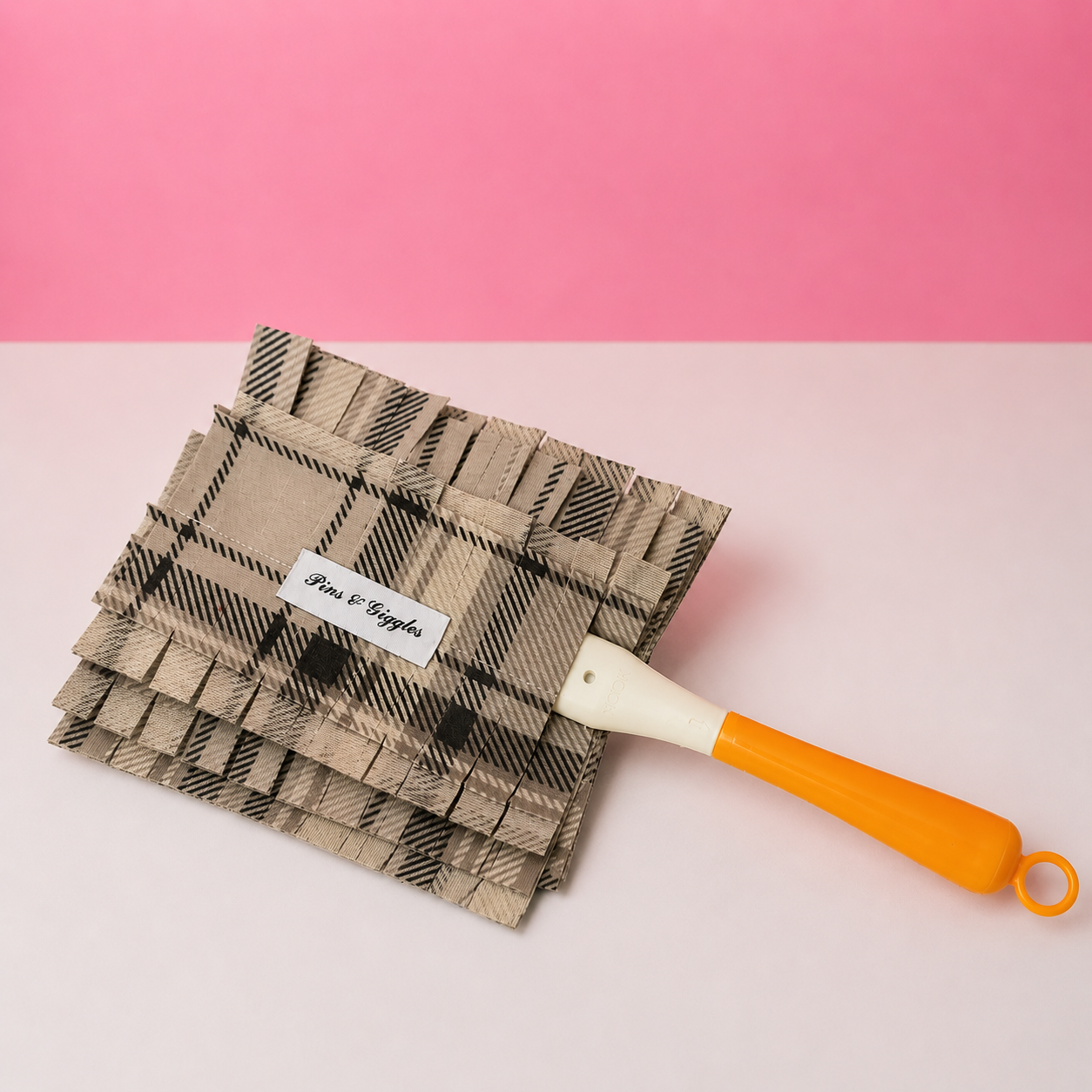 Neutral plaid swiffer duster cover with a yellow-handle on a pink and white background