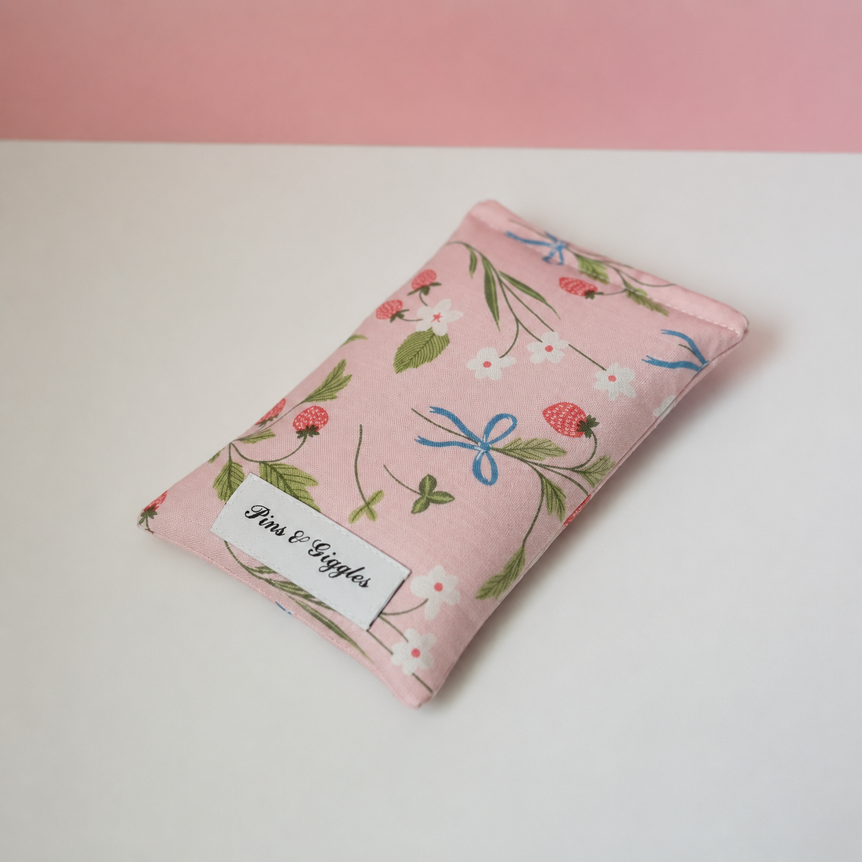 Floral-patterned pink pouch with a label on a white surface