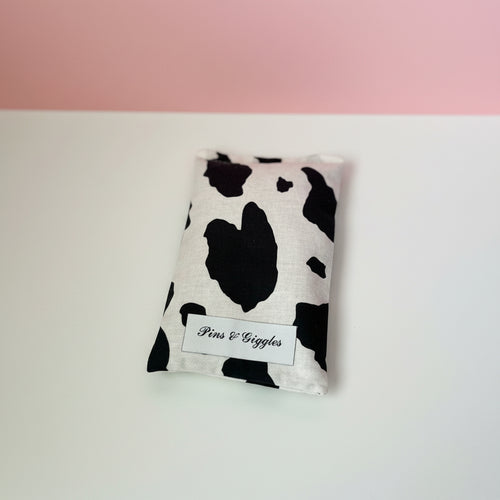 Cow print pouch with 'Pins & giggles' label on a white surface with pink background