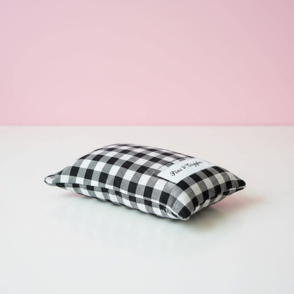 Black and white checkered pouch with 'Pins & Giggles' label on a white surface