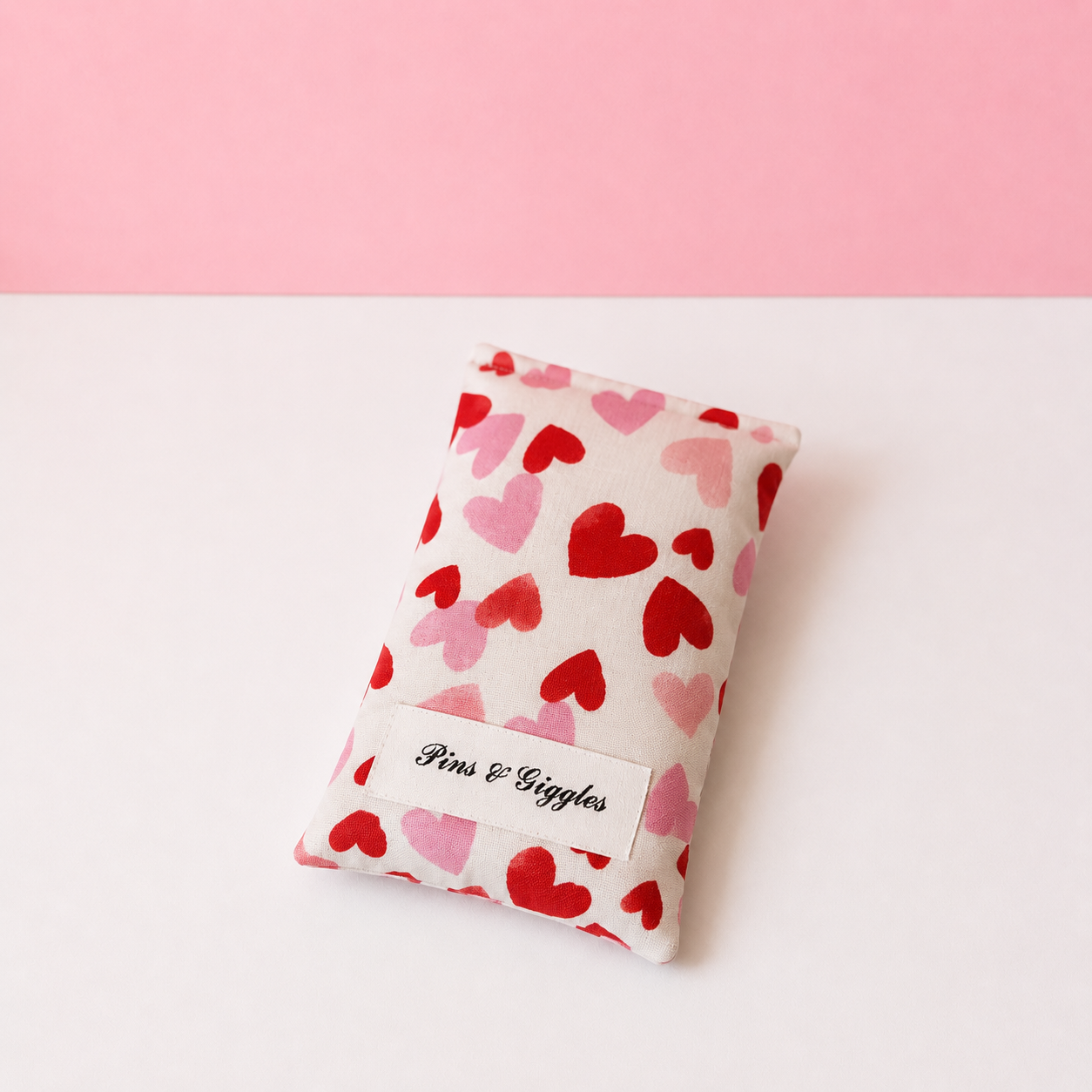 pouch with red and pink heart pattern on a white surface, branded 'Pins & Giggles'.
