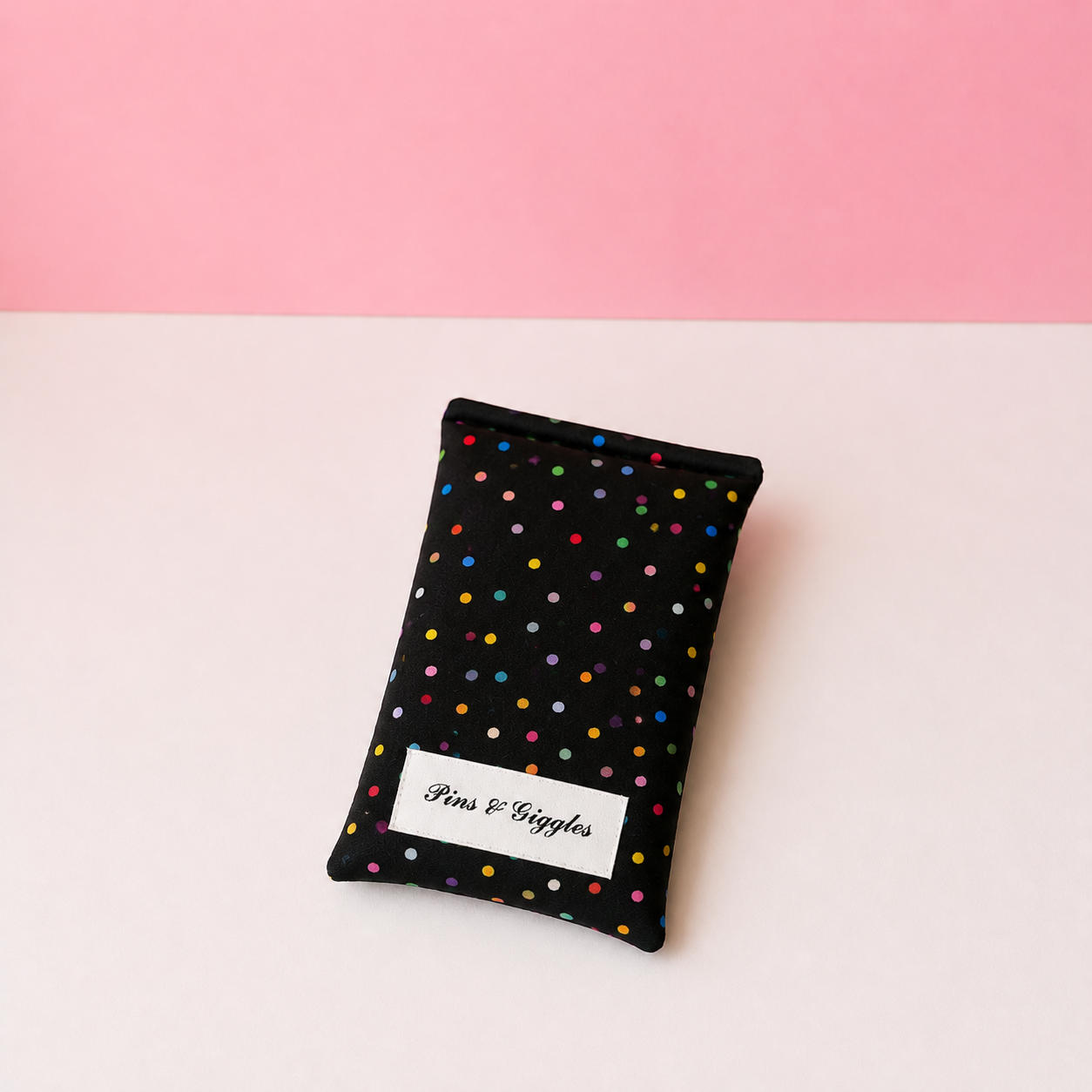 Black fabric pouch with colorful polka dots and 'Pans & Giggles' label on a pink and white background