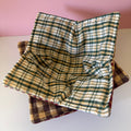 Two rustic colored plaid or checkered fabric bowls stacked on a white surface with a pink background