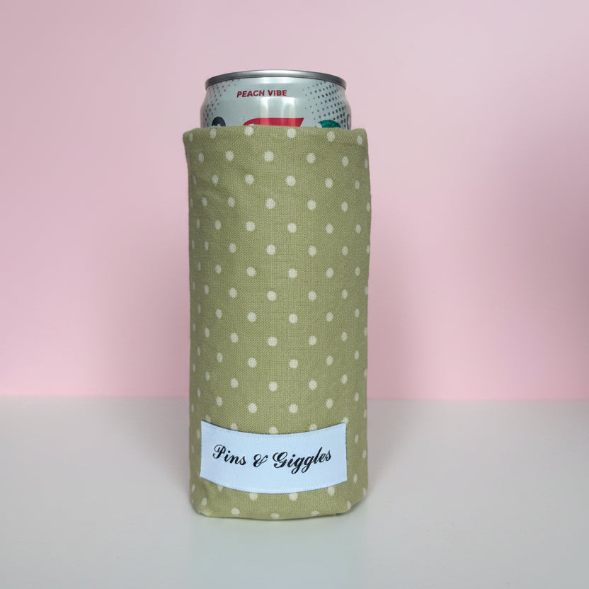 Green can cooler with white polka dots and 'Pins & giggles' label on a pink background