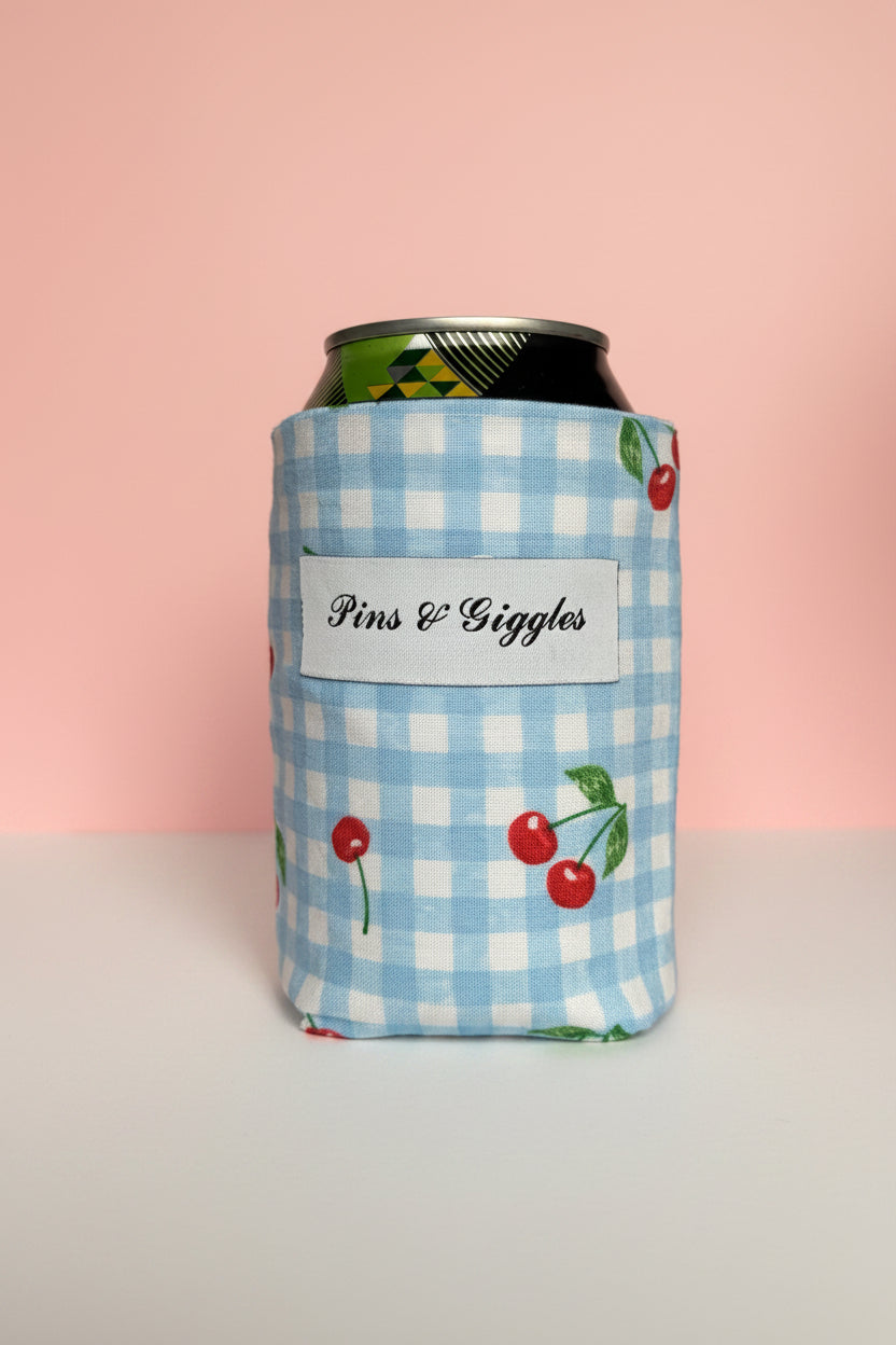 Can cooler with blue checkered pattern and cherry design on a pink background