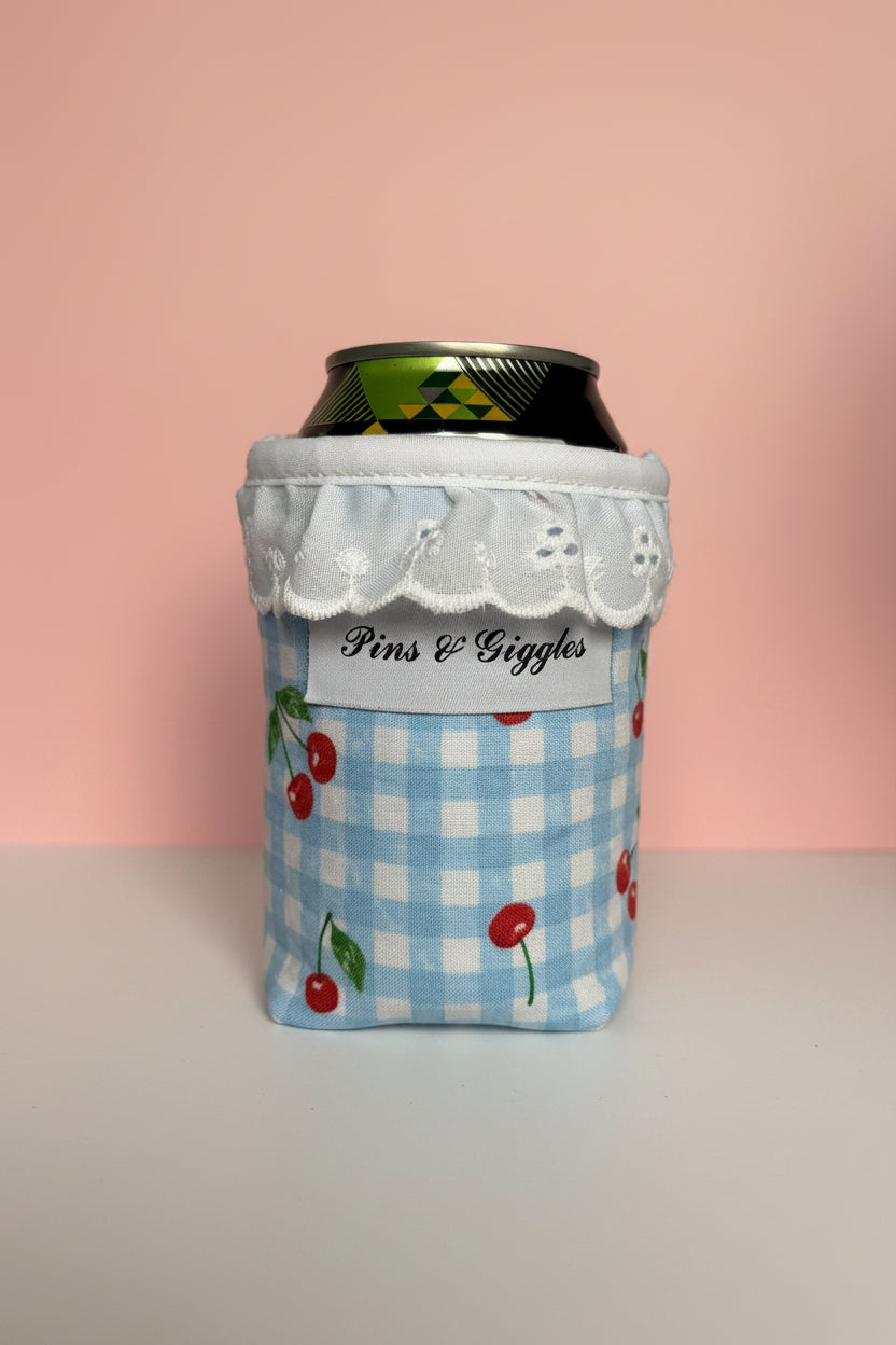 Can cooler with cherry design and 'Pins & Giggles' branding on a pink background