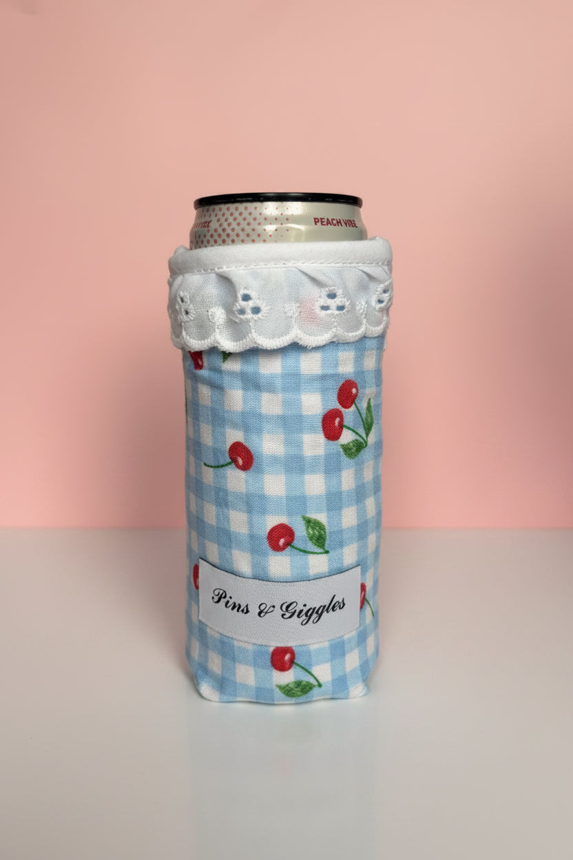 Can cooler with blue checkered pattern and cherry design with a pink background