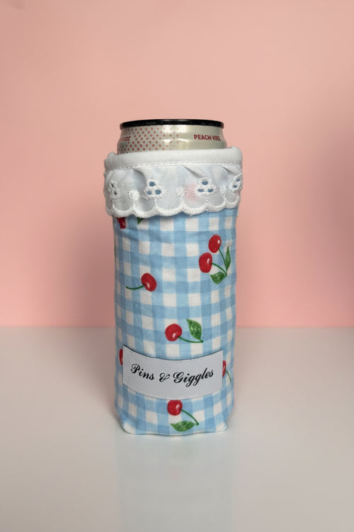 Can cooler with blue checkered pattern and cherry design with a pink background