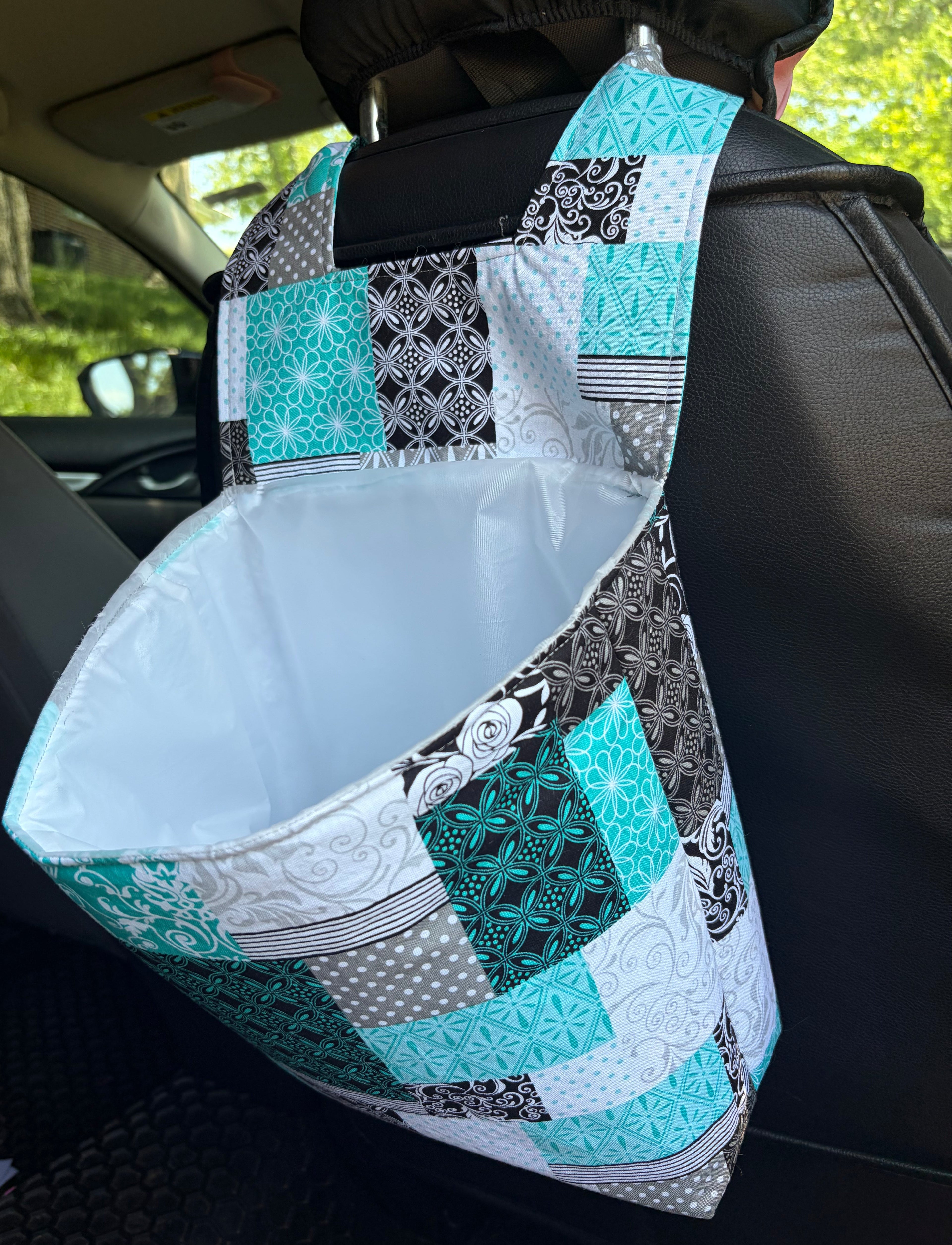 Car headrest cover with a patchwork design in teal, black, and white on a car seat.