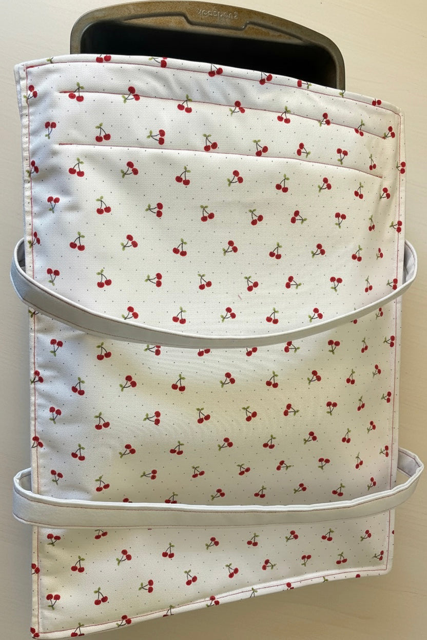 White fabric casserole carrier with cherry pattern background and a 9x13 pan mostly in.
