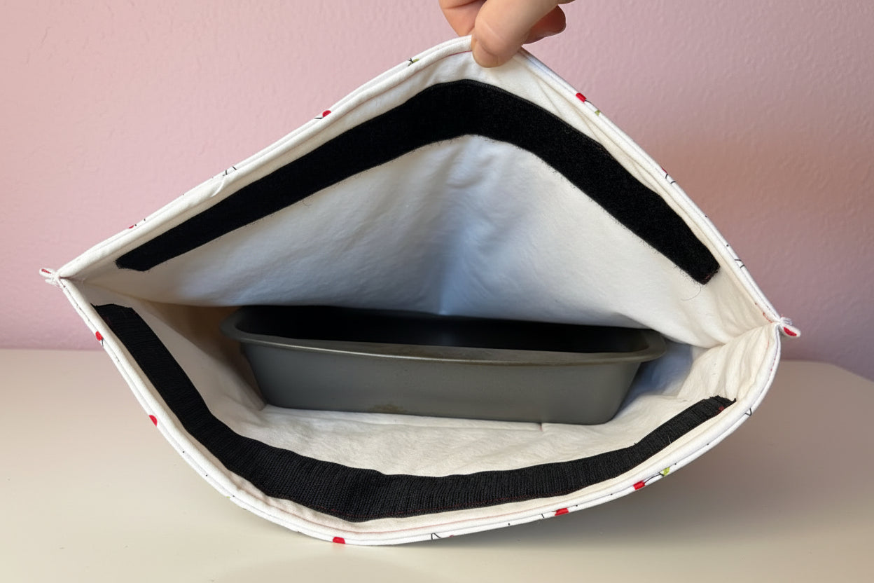 Open casserole carrier with a gray pan inside against a pink background