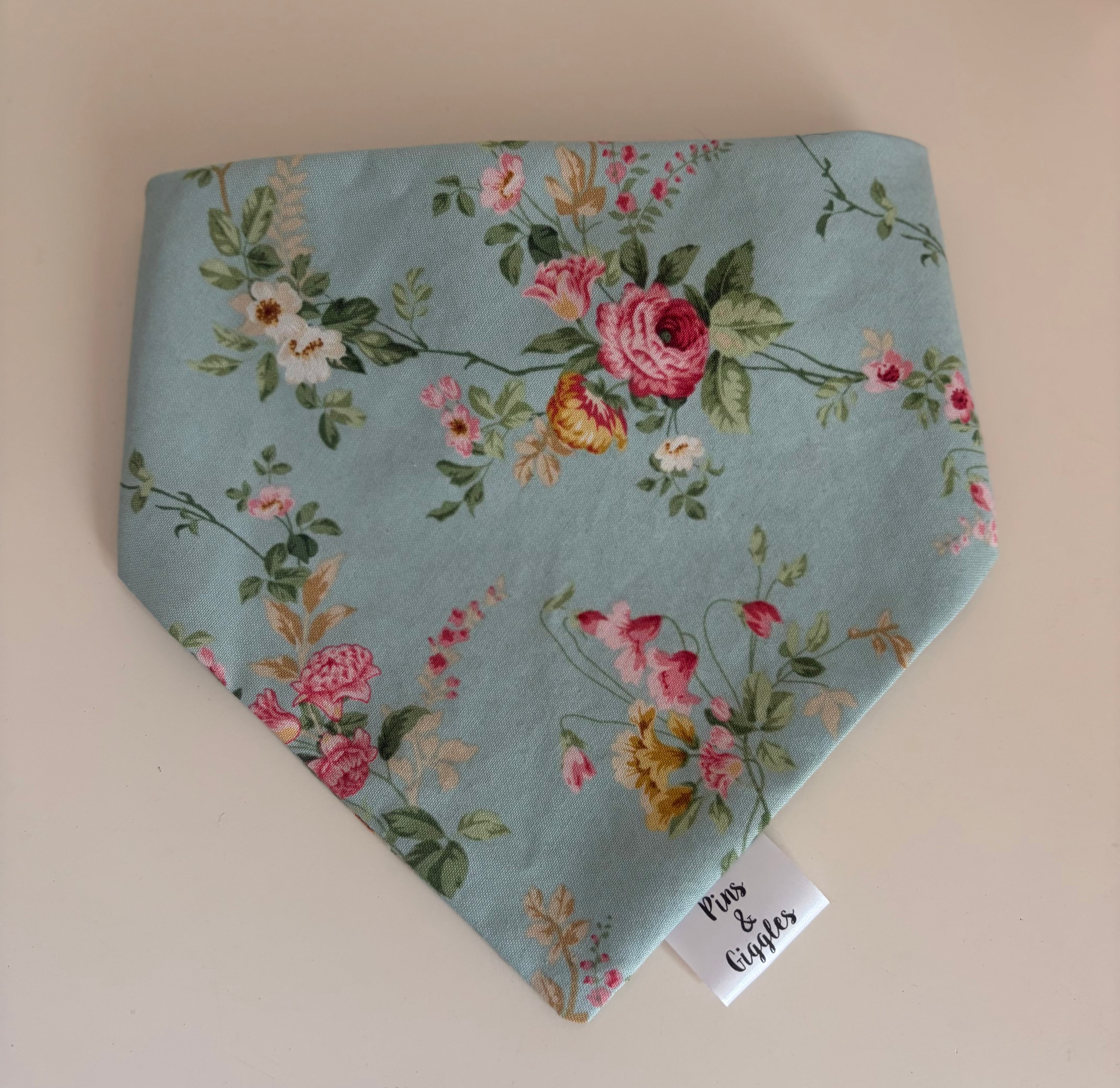 Floral patterned bandana on a beige background with a visible brand tag.