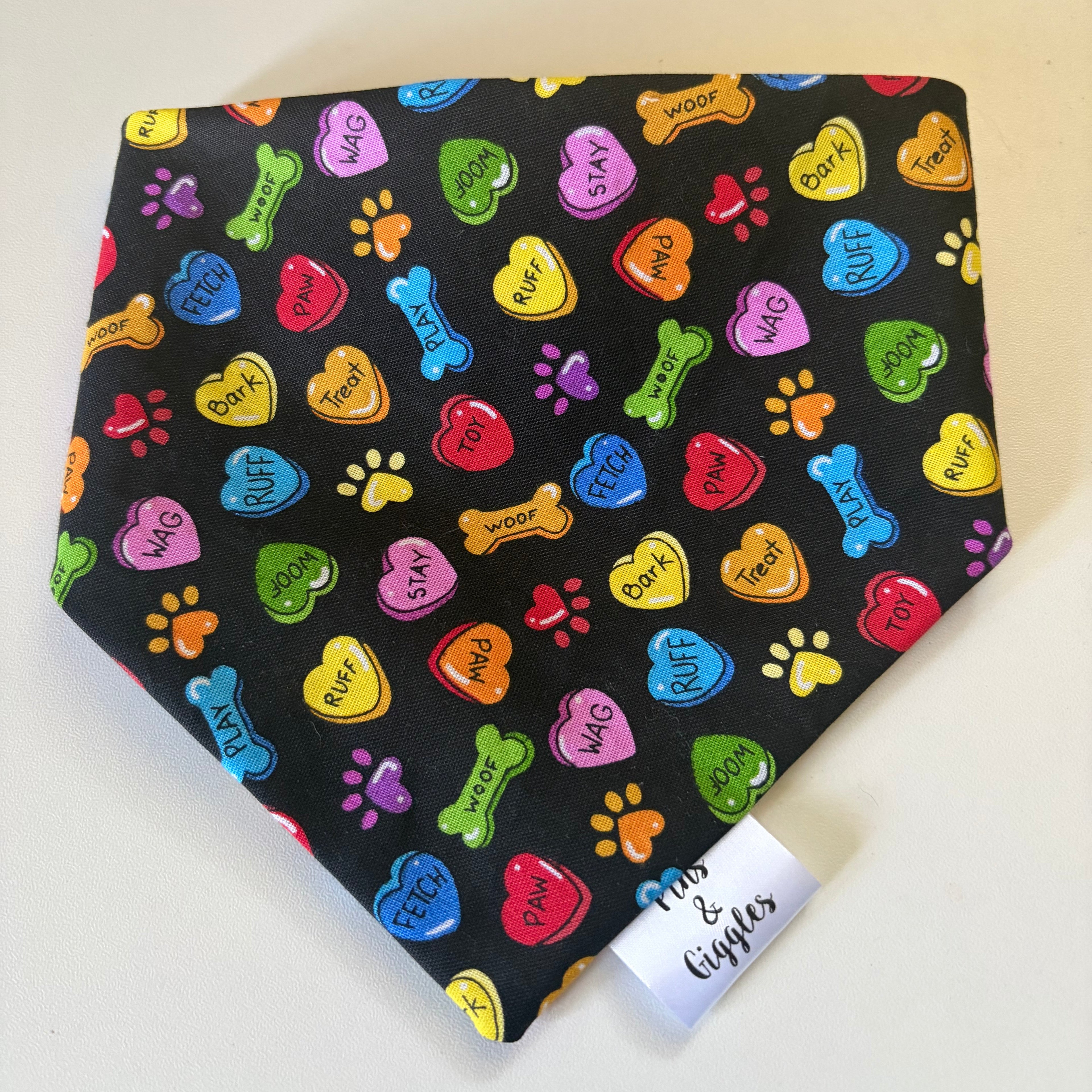 Colorful dog bandana with text and patterns on a black background, displayed on a white surface.