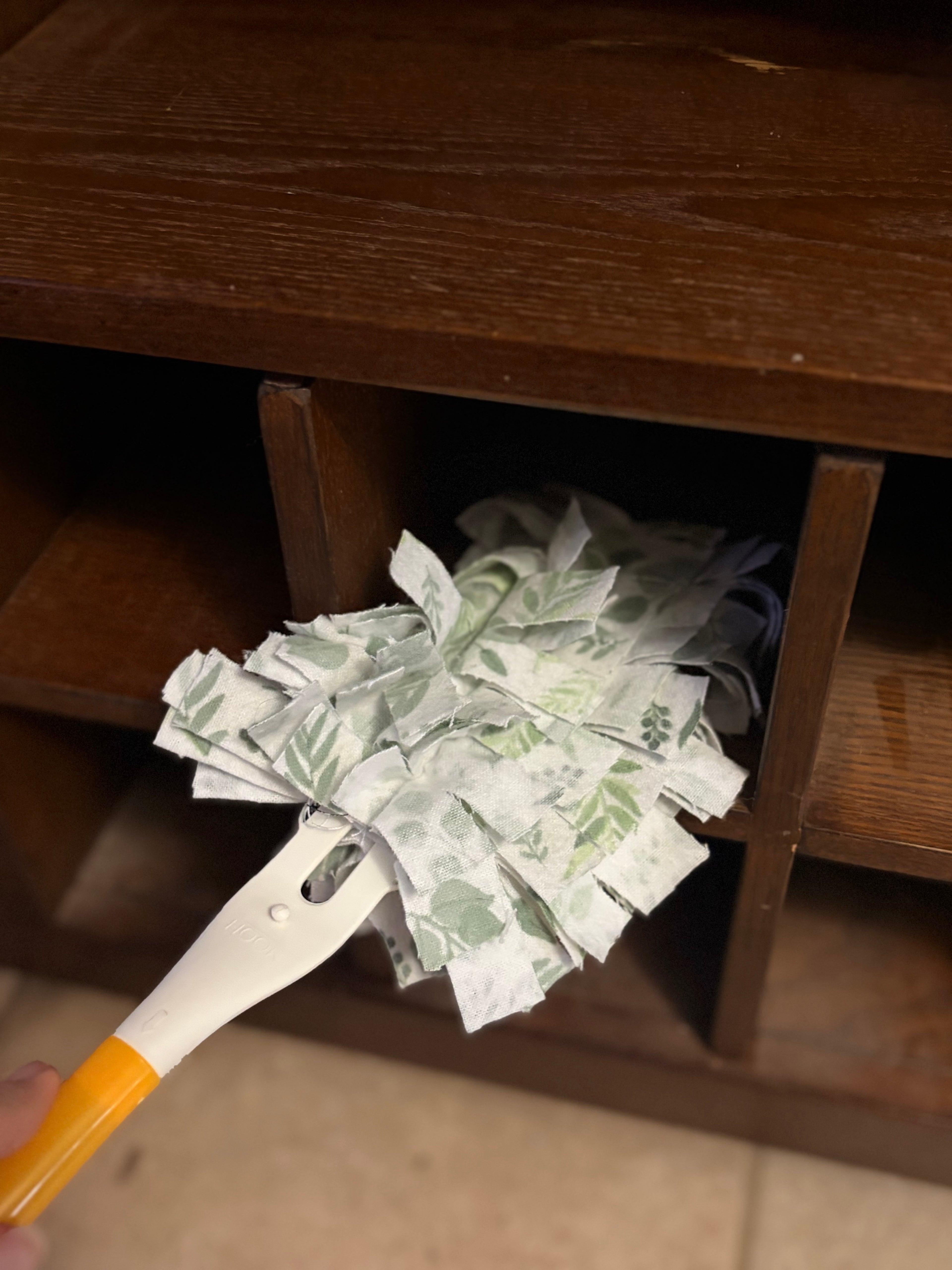 Fanned-out cloth duster held by a yellow handle against a wooden background