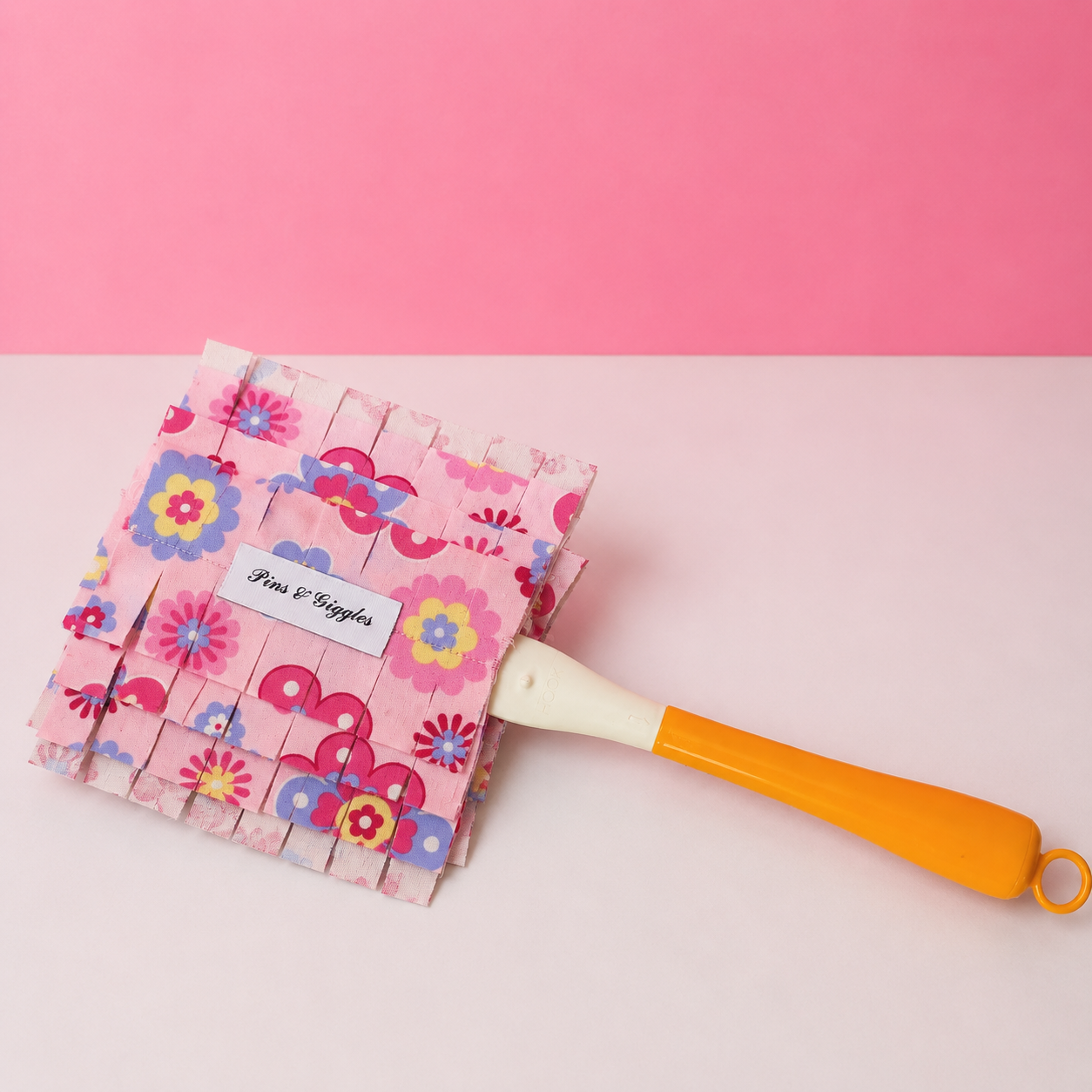 pink flower-patterned swiffer duster cover with a yellow-handle on a pink and white background