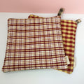 Two checkered potholders sitting on a wooden surface with a pink background