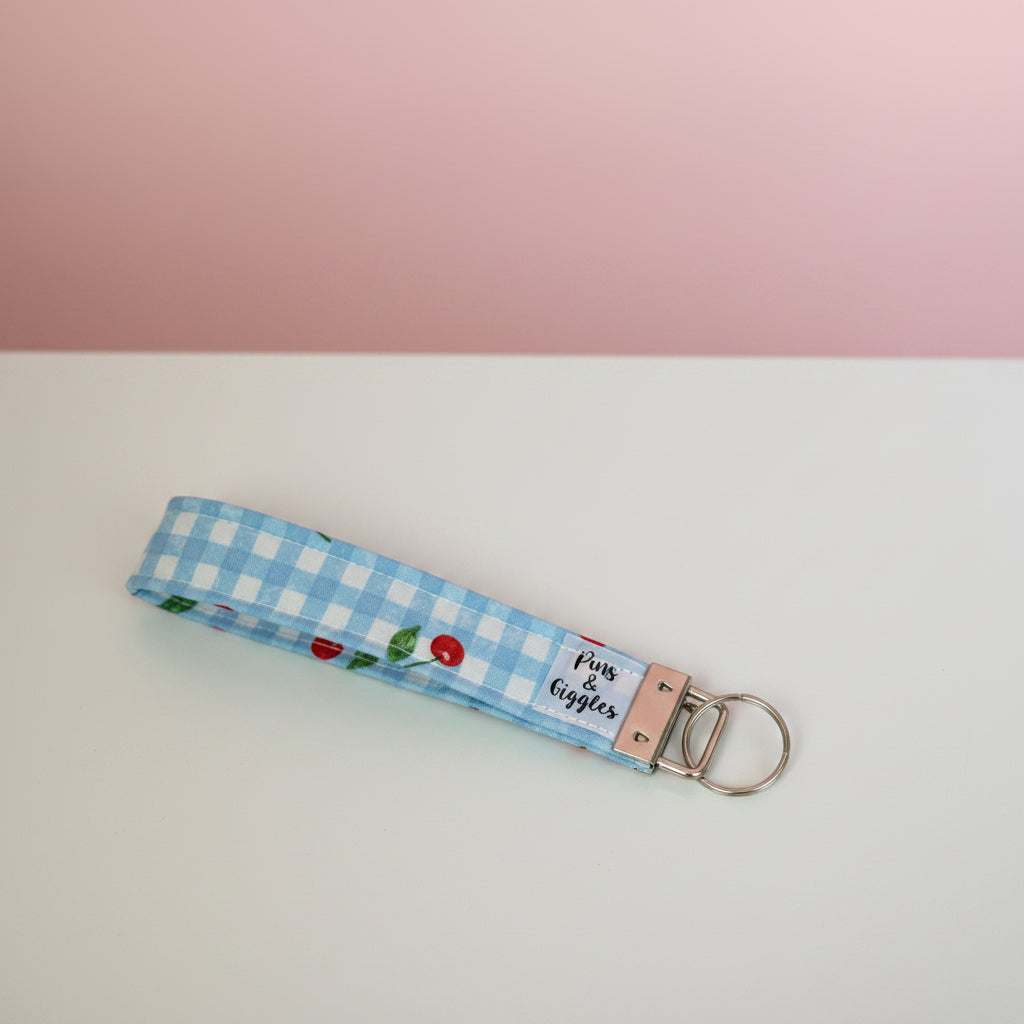 Keychain with blue checkered and cherries pattern on a white surface