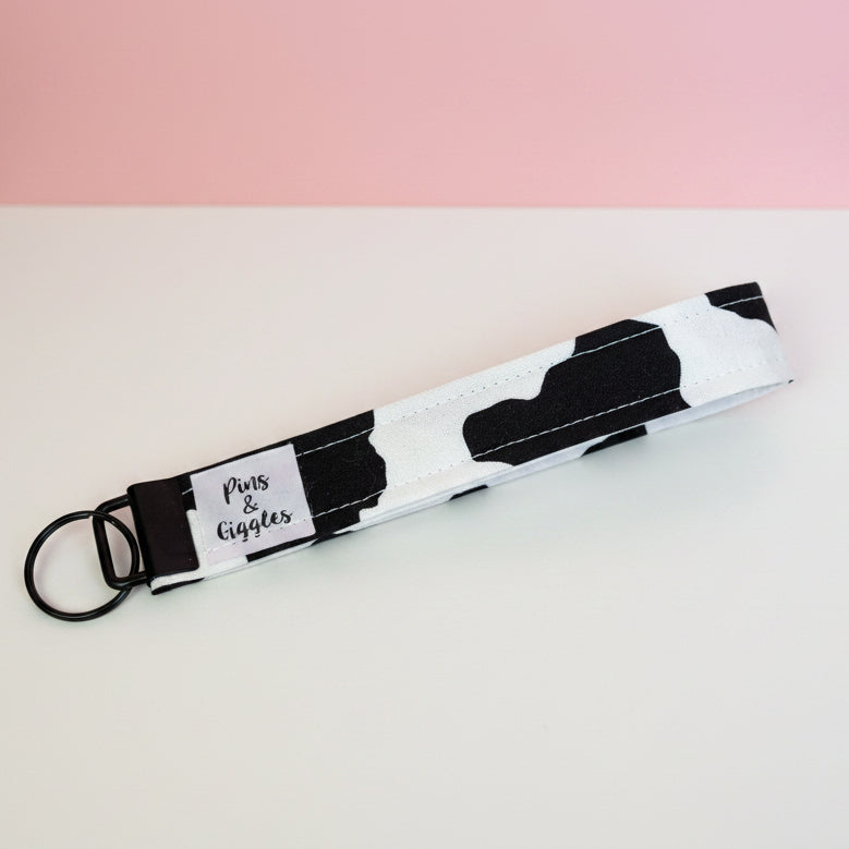 Black and white patterned keychain with a keyring on a white surface and pink background