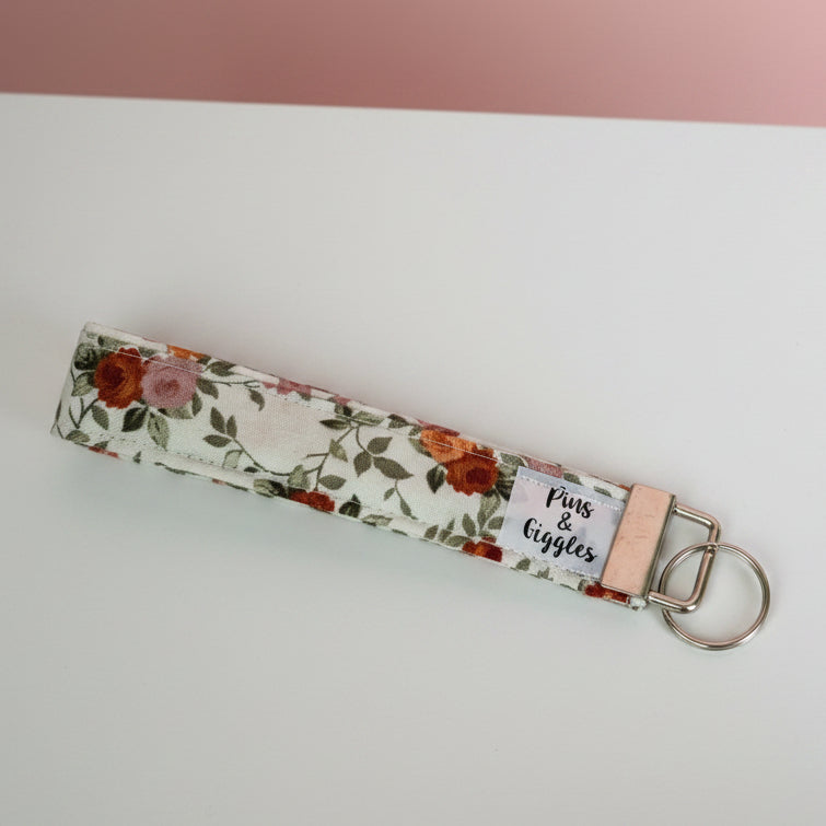 Floral keychain strap on a white surface with a pink background